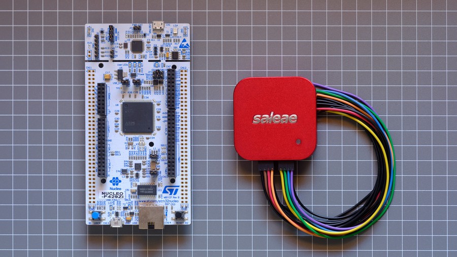 White STM32F4 microcontroller PCB next to red Saleae Logic analyser